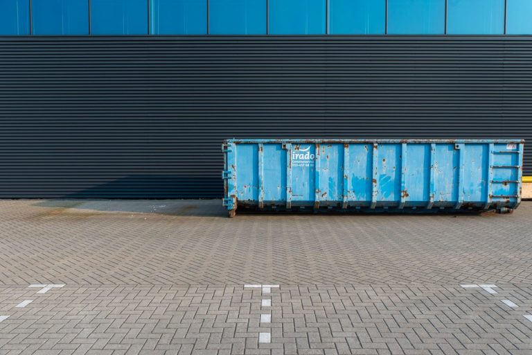 Blue open-top roll-off dumpster parked beside a modern building