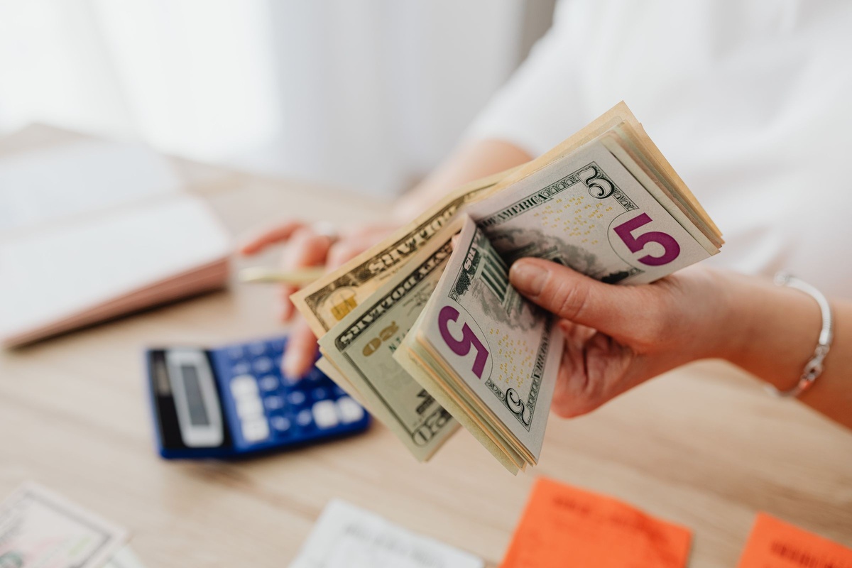 Hands counting US dollar bills next to a calculator while working out a dumpster rental estimate