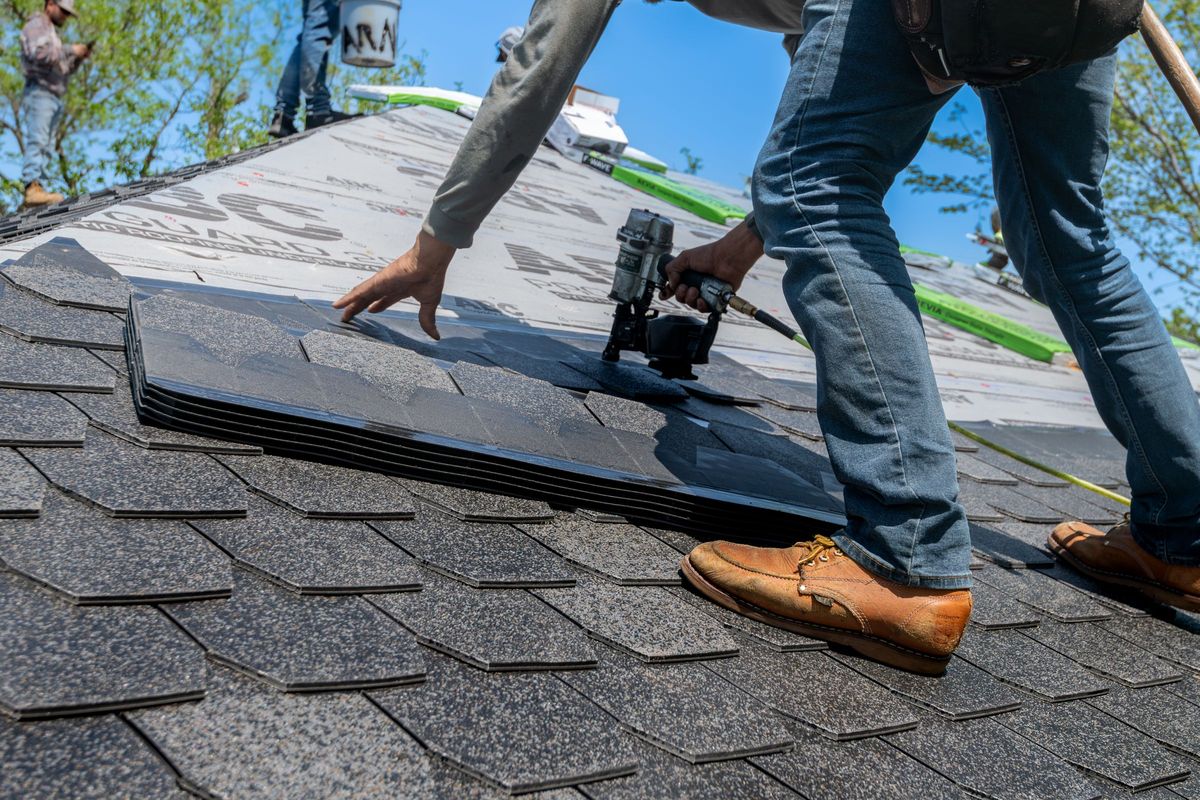 Roofer using a nail gun to install asphalt shingles