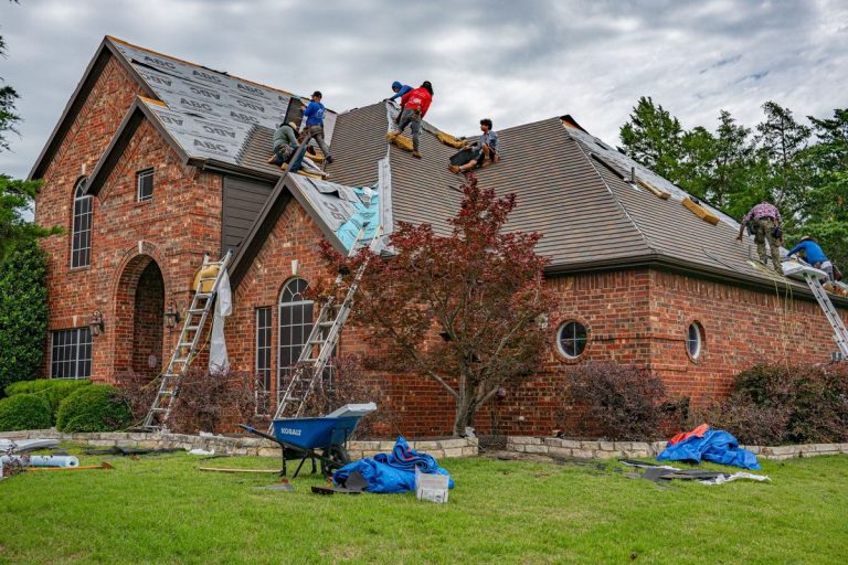 Roofers working on a house roof re-roof job with materials on the lawn
