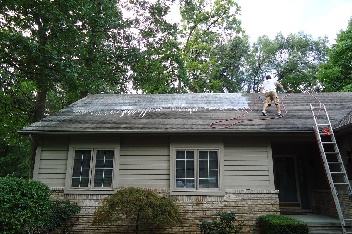 Worker on a worn asphalt shingle roof of a single-story house before re-roofing